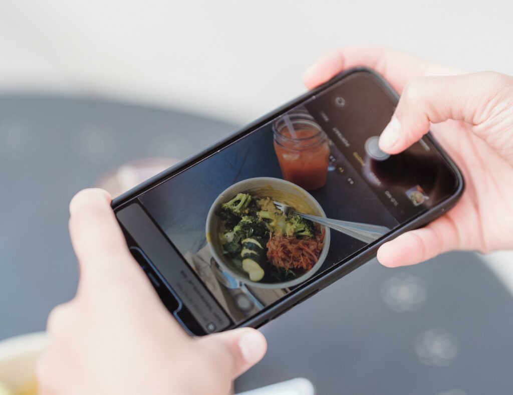 Hand holding a smartphone filming a bowl of food, symbolizing the capture of a product instead of a personal video testimonial for a company.