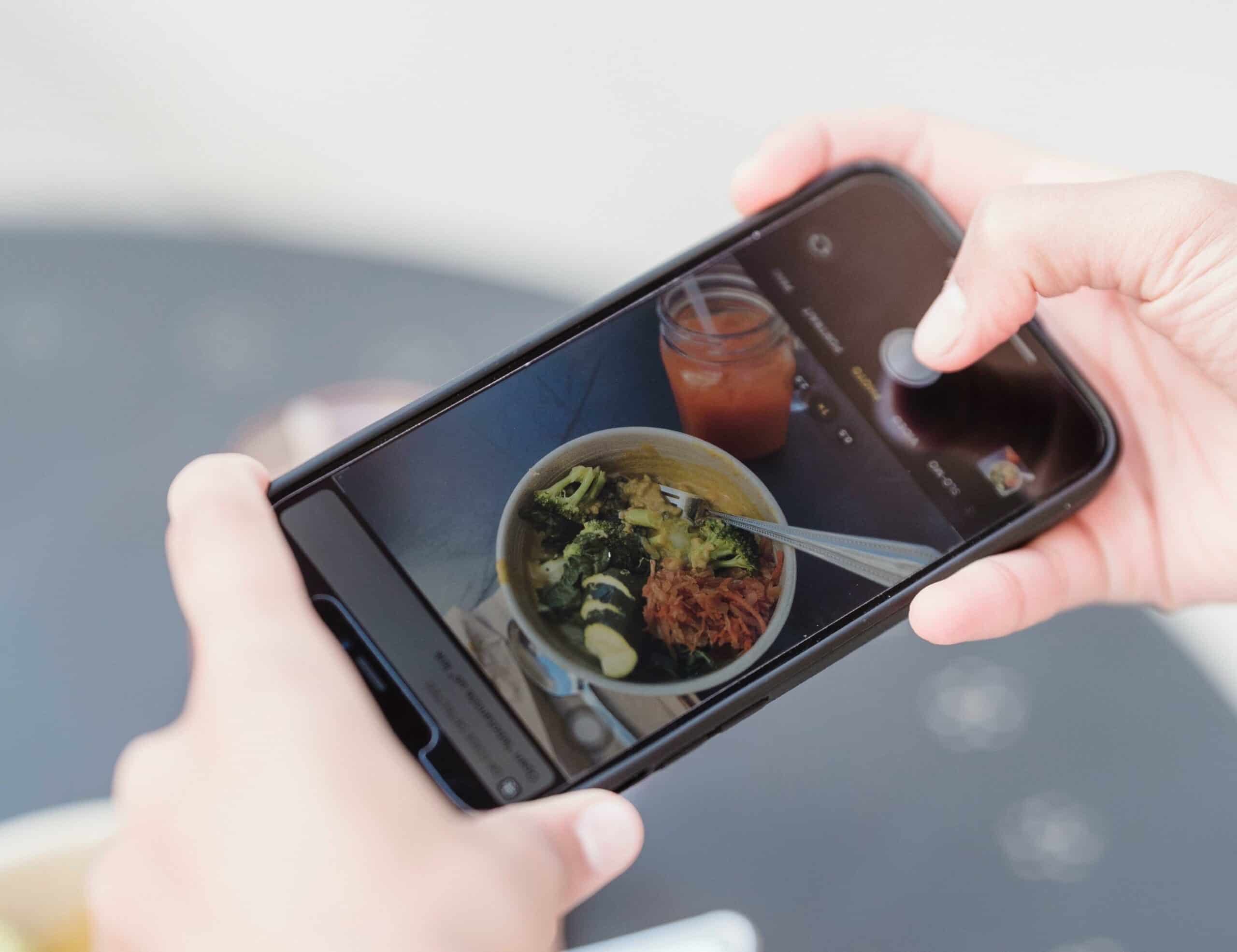 Main tenant un smartphone en train de filmer un bol de nourriture, symbolisant la capture d'un produit au lieu d'un témoignage vidéo personnel pour une entreprise.